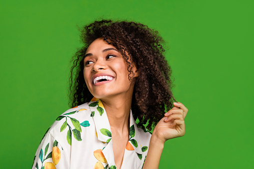 Photo of shiny sweet lady wear print shirt smiling looking empty space holding hair curl isolated green color background.