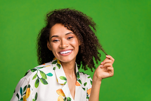 Photo of girly shiny lady wear print shirt smiling holding hair curl empty space isolated green color background.