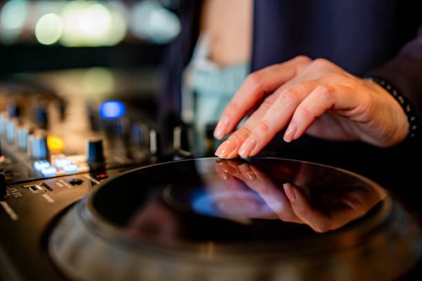 istock close-up of hands skillfully adjusting knobs and sliders on a professional DJ mixer, illuminated by colorful lights. The mood conveys focus and control during a live music event 2050595043
