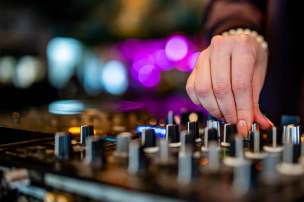 istock close-up of hands skillfully adjusting knobs and sliders on a professional DJ mixer, illuminated by colorful lights. The mood conveys focus and control during a live music event 2050595558