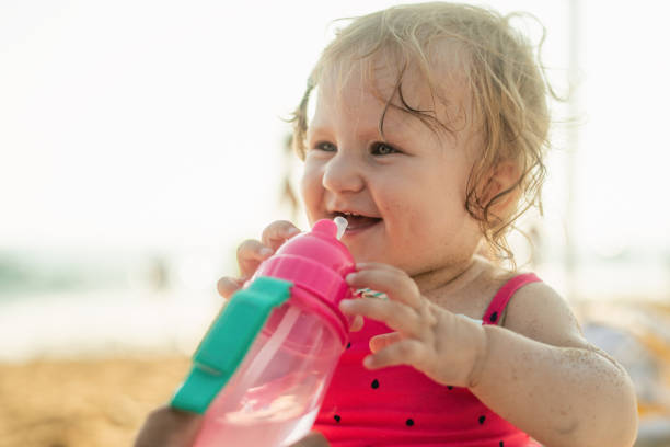 Baby girl caucasian 2 years old drinks water in summer in hot weather in a baby stroller.