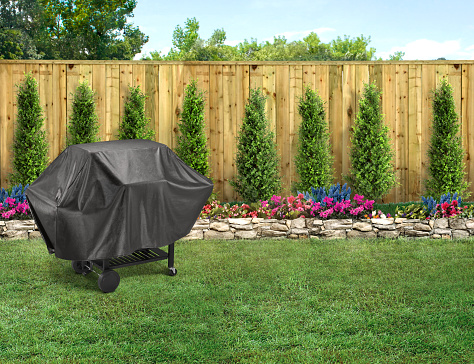 Covered bbq grill in a backyard with green grass and wood fence