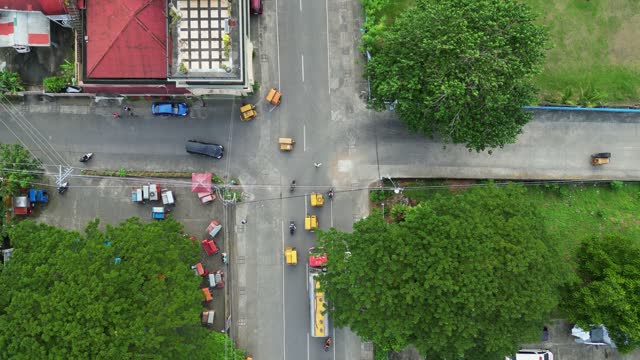 Aerial top down view of cargo truck and tricycles driving on rural provincial streets and intersection in quaint Philippine town.