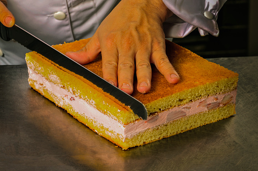 chef cutting a cake with a knife, closeup of hands