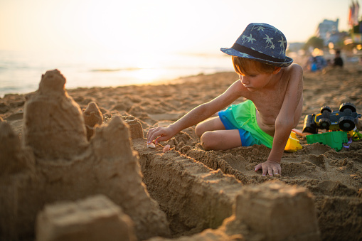 Little boy building sandcastle on the beach on summer holidays
