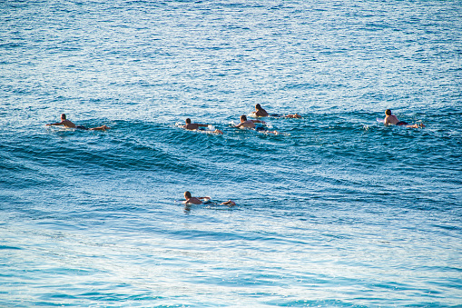 Bali, Uluwatu - Surfers floating on their boards, waiting for waves. The ocean’s varying shades of blue create a textured background. The image captures the calm before the surf.