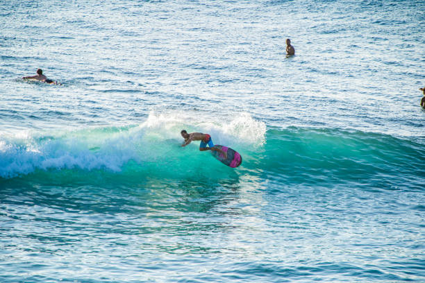 Bali, Uluwatu - A surfer, balanced on a surfboard, rides a turquoise wave. The clear blue ocean serves as a vibrant backdrop.
