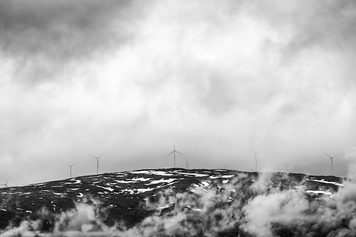 In a play of shadows and light, the silhouettes of wind turbines stand atop a Norwegian ridge, piercing the swirling mists in this atmospheric black and white photo