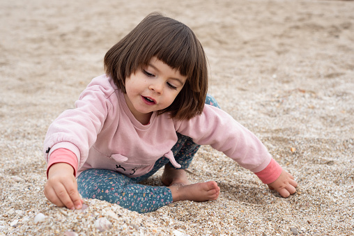 Little girl playing with sand at a beach  in a winter day