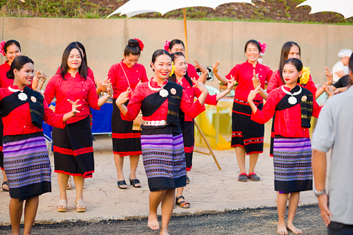 Adult thai women start dancing rum thai in public for people. Women are wearing traditional clothing. They are dancing barefoot. Scene is at a market and local festical below King Naresuan monument in Lampang. Women are cheerful and laughing and smiling