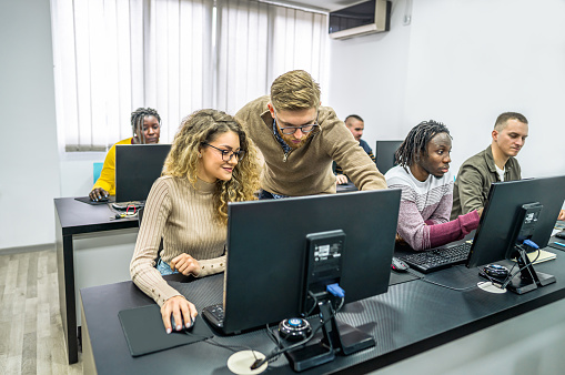 A young male teacher helping young student to find a solution in a programming class