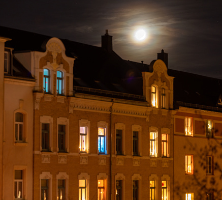 Panoramic view of the moon when it illuminates through thins clouds the neighborhood buildings during a full moon winter night.
