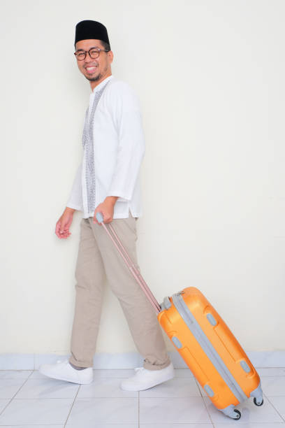 istock Full body portrait of Moslem man walking and pulling suitcase with happy expression 2050682124