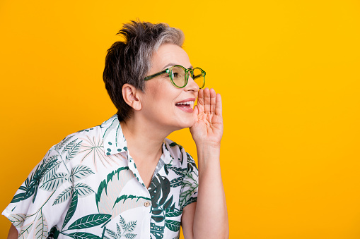 Photo portrait of lovely grandma cover mouth share secret dressed stylish tropical print garment isolated on yellow color background.