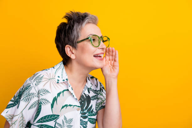 Photo portrait of lovely grandma cover mouth share secret dressed stylish tropical print garment isolated on yellow color background Photo portrait of lovely grandma cover mouth share secret dressed stylish tropical print garment isolated on yellow color background. whisperer pictures stock pictures, royalty-free photos & images