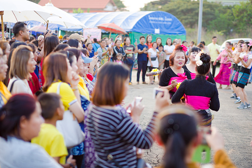Mature thai women dancing with mortar and pestle captured in Lampang. Scene is close to and below King Naresuan monument in Lampang. Dancing women dance with joy. Many thai people are standing  at left side and in background. People are taking videos with mobile phones