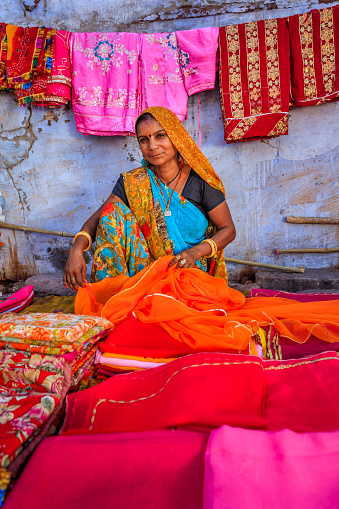 Indian woman selling colorful fabrics on local bazaar, Jodhpur, Rajasthan, India. Jodhpur is known as the Blue City due to the vivid blue-painted houses around the Mehrangarh Fort.