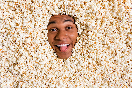 Photo of positive funny guy have spend free time weekend watch tv television film show tongue out isolated pop corn background.
