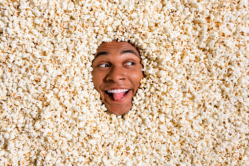 Photo of carefree funky guy look empty space advert cinema tickets bargain enjoy show tongue out isolated pop corn background.