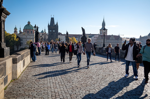 A photo of tourists crossing the Charles Bridge in Prague, Czech Republic.  The Charles Bridge is a medieval stone arch bridge that crosses the Vltava River in Prague and was constructed in 1357.