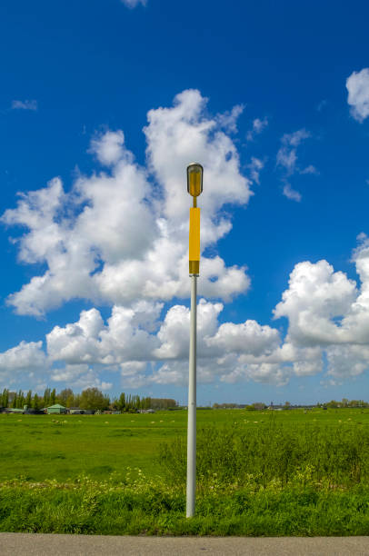Street light on a background of blue sky with clouds and a flat green meadow in The Netherlands.