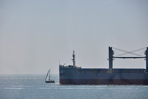 Small sailboat just in front of a large tanker ship