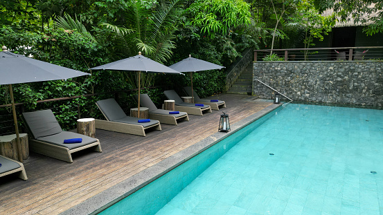 Lounger with parasol on terrace by swimming pool among tropical rainforest and the lake in the resort. Summer and holiday concept