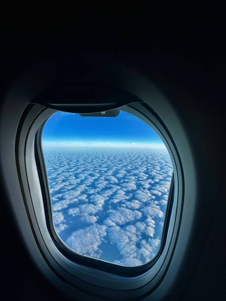 looking out a commercial aircraft window at altocumulus clouds blanketing a blue sky