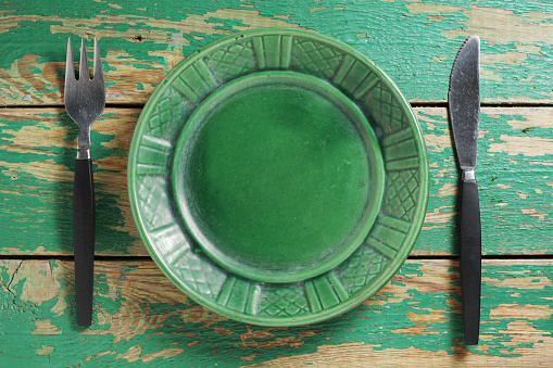Green plate with fork and knife on old wooden background, top view