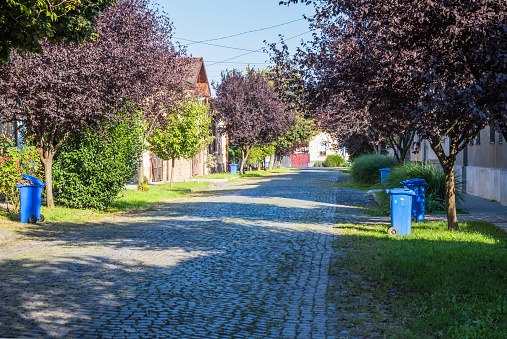 Blue garbage cans on the street in a small town near every house. Centralized garbage collection in a small cozy European city. Garbage collection on a certain day of the week.