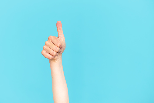 Cropped view of human hand showing thumb up gesture isolated on blue copy space background. Approve advertising concepts, business deal, good client service make positive feedback