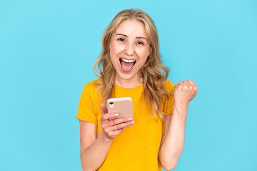 Overjoyed woman received good news or unexpected message on cellphone, job promotion or big discount sale. Excited young female rejoicing success, showing yes gesture, satisfying from win