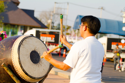 Performing male thai musician with big drum. Man is exercising in public in Lampang. Man is part of drummers who are doing rehearsal for drum event in evening free for public. Drumming is popular music event in Lampang.