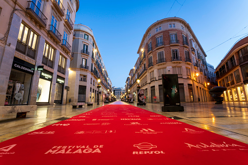 Malaga, Andalusia, Spain - March 1, 2024.  Larios Street in Old Town, the city center of Malaga with the Festival de Málaga logo on the red carpet to promote the annual Malaga Film Festival that offers movie screenings and an award ceremony in Malaga, Costa del Sol, Spain. Stone lined streets with beautiful Spanish buildings and shops will soon be filled with celebrities, movie stars, actors, actresses, fans and photographers all lined up along the red carpet walk. Malaga is preparing for the publicity event, celebration and crowds.