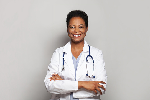 Happy successful doctor woman medical worker in white lab coat standing with crossed arms on white background