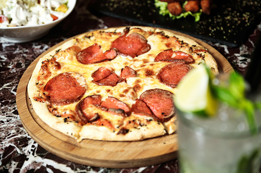 A photo featuring a pepperoni pizza placed on a cutting board alongside a refreshing drink.