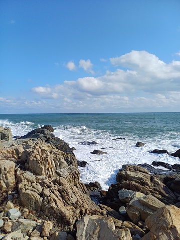 A seascape of a summer beach with blue sky and clouds. The waves and rocks create a magnificent view.