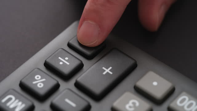 A man pressing the equals button on a calculator with his pointer finger.
