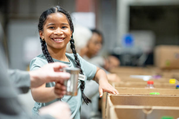 Packing Donations A sweet mixed race girl helps her family work together at a local food bank, packing donations. She is dressed casually and cheerfully helping. food bank stock pictures, royalty-free photos & images