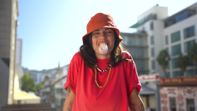 Portrait of nonbinary person in red hat blowing gum on balcony