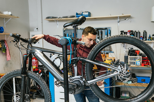 The mechanic checks the brake and rear gear shift of a mountain bike in his workshop