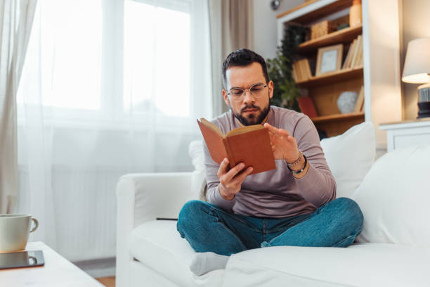 istock Handsome man reading a book in his living room 2051061435