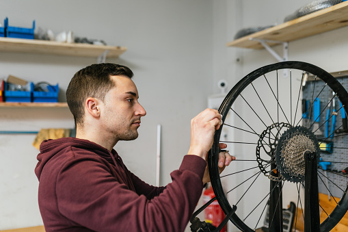 The bike mechanic checks and repairs the rear wheel rim and spokes of a bicycle in his bike workshop.