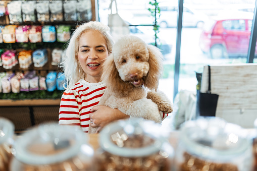 Young woman with poodle in pet shop buying food