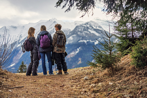 Family hiking in the Alps, Salzburg, Austria. They are standing on a path and enjoying the snow and the spectacular view of the snowcapped High Tauern mountains.
Overcast winter day, its snowing.
Shot with Canon R5