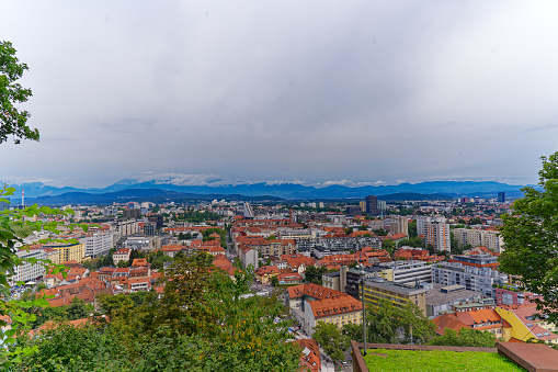 Aerial view of City of Ljubljana seen from castle hill with mountain panorama in the background on a cloudy summer day. Photo taken August 9th, 2023, Ljubljana, Slovenia.