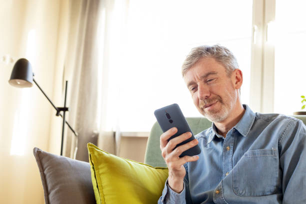 istock 50 year old man sitting on the sofa in his home using a smart phone 2051200030