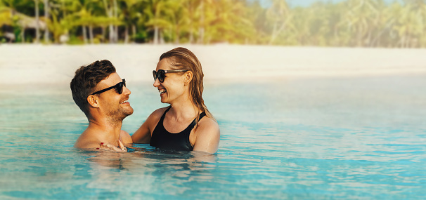 happy couple in love swimming in the ocean by tropical white sand beach. romantic getaway. banner with copy space