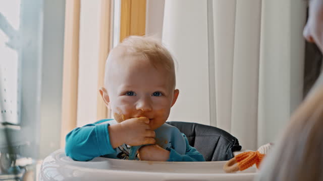 Toddler Boy Eating Food on Pacifier while Sitting in Baby Walker by Mother at Home