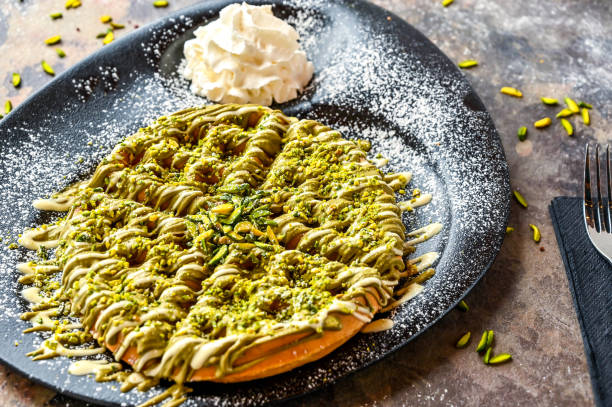 Pistachio Waffle with chocolate, whipped cream, knife and fork served in dish isolated on dark background top view cafe dessert food